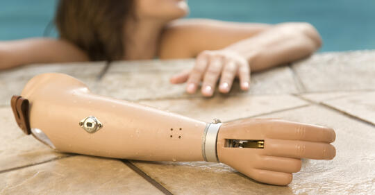 Armprotese som ligger på kant av svømmebasseng med dame i vannet i bakgrunnen